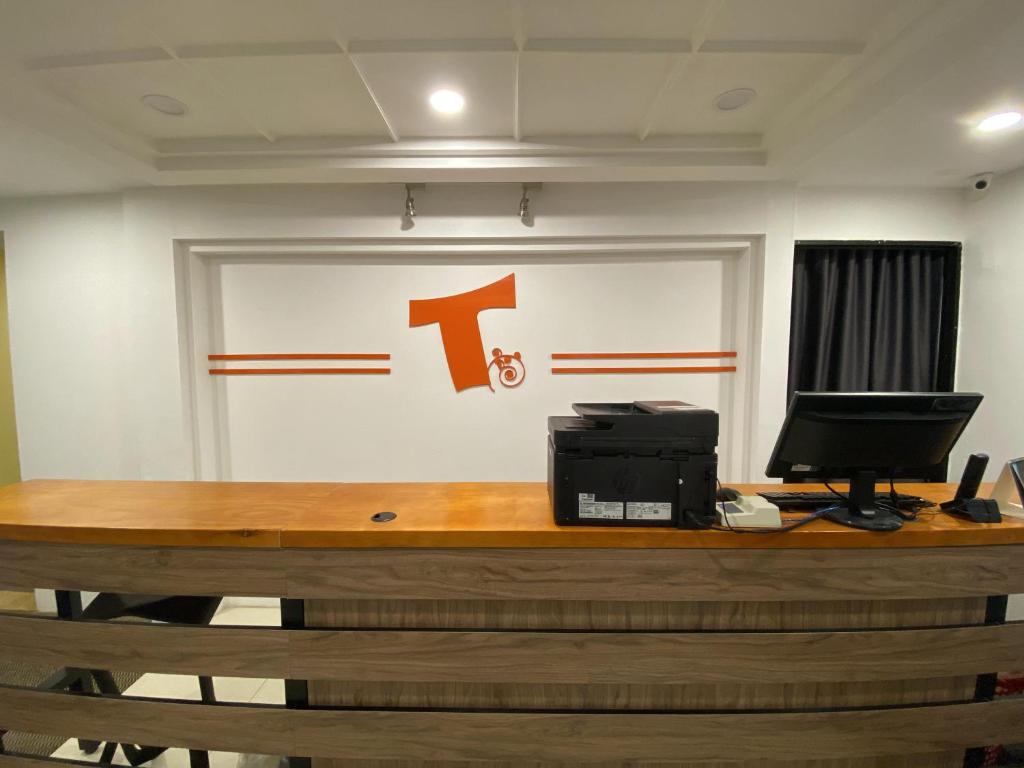 a desk with a computer and a sign on a wall at T Hotel Jalan Sultanah in Alor Setar
