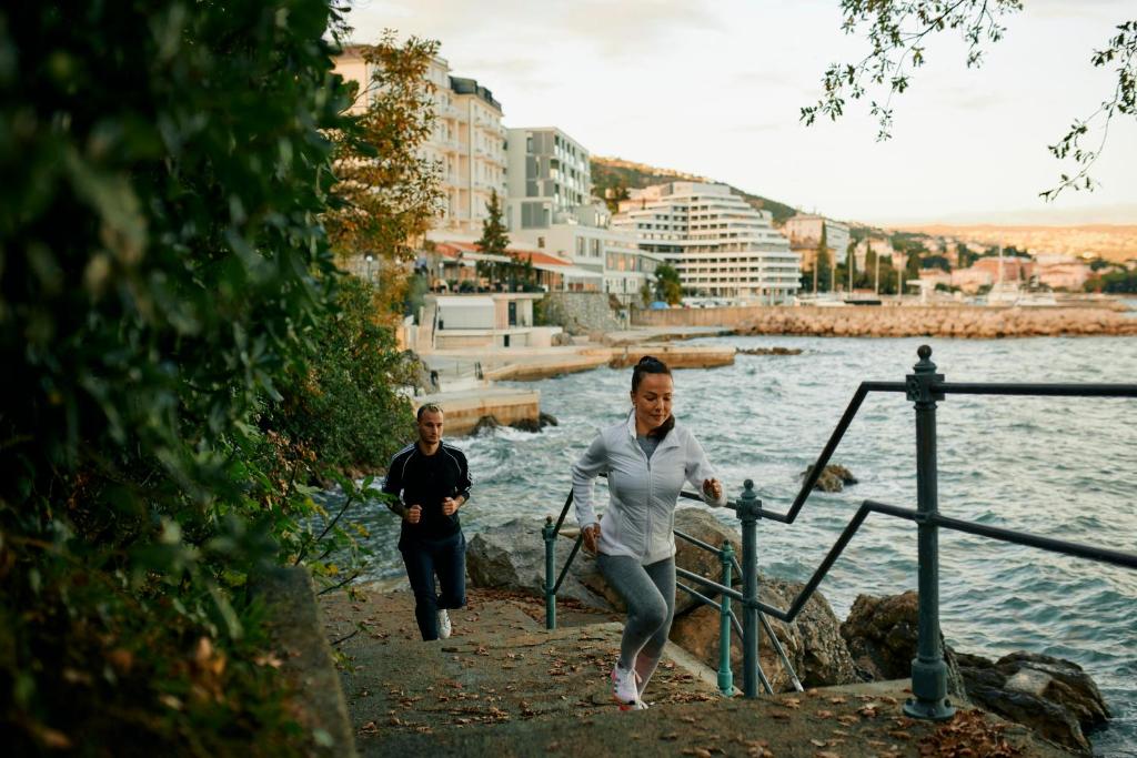 two people walking down a path by the water at Hotel Istra - Liburnia in Opatija