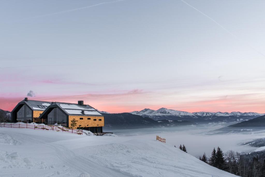 a building on top of a snow covered hill with a mountain at Hüttendorf Schlögelberger in Sankt Margarethen im Lungau