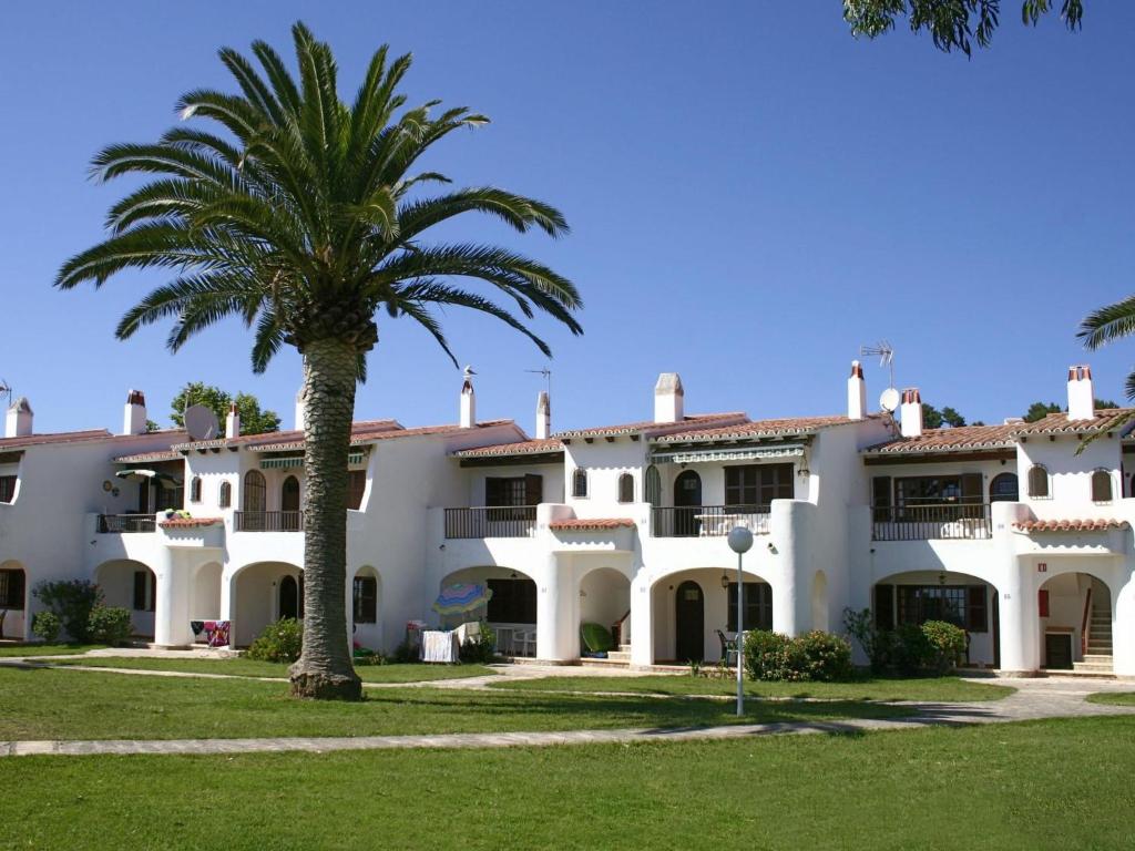a large white building with a palm tree at Apartment Son Bou Gardens PLUS by Interhome in Son Bou