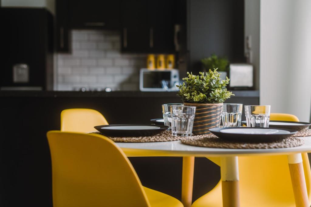 a table with plates and glasses on it with yellow chairs at SleepWell Apartments in Glasgow