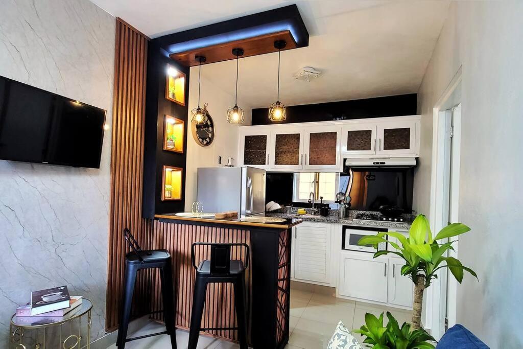 a kitchen with white cabinets and a bar with stools at Apartamento acogedor Ashmi in Santiago de los Caballeros