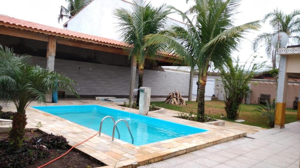 a swimming pool in front of a house with palm trees at Piscina 6 QUARTOS 300mPRAIA jardim churrasqueira 16 PESSOAS garagem 3 carros Monitoramento 24 horas Mesa de sinuca in Itanhaém