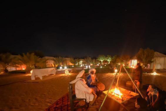 um grupo de pessoas sentadas num banco ao lado de um incêndio em sunset luxury camp em Merzouga