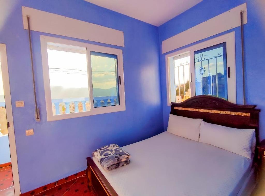 a blue bedroom with a bed and two windows at Dar Khairoun with Balcony in Chefchaouene