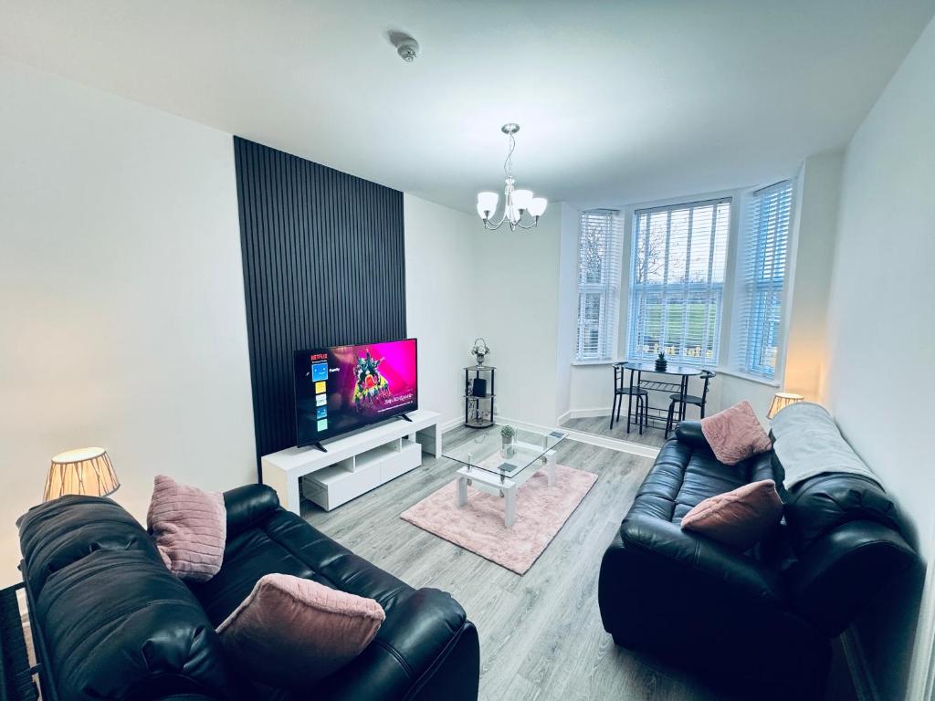 a living room with a black leather couch and a flat screen tv at Spanish City View, Stylish Sea Front Apartment Free Onsite Parking in Whitley Bay