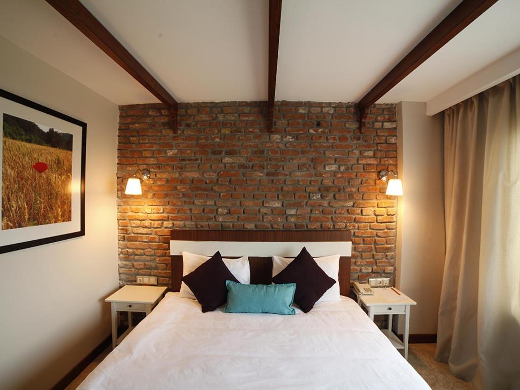 a bedroom with a white bed with a brick wall at Hotel Milestone1915 in Gelibolu