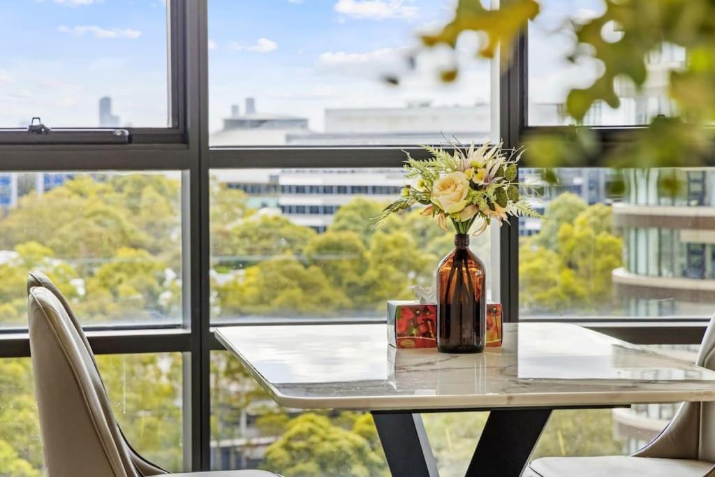 eine Vase mit Blumen auf einem Tisch vor einem Fenster in der Unterkunft Warm and cozy 3 Bed APT in Sydney