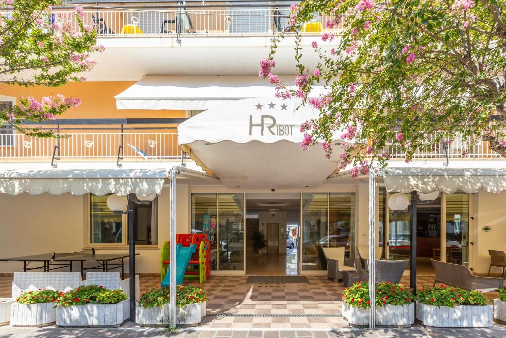 uma entrada do hotel com mesas e cadeiras e um guarda-sol em Hotel Ribot em Rimini