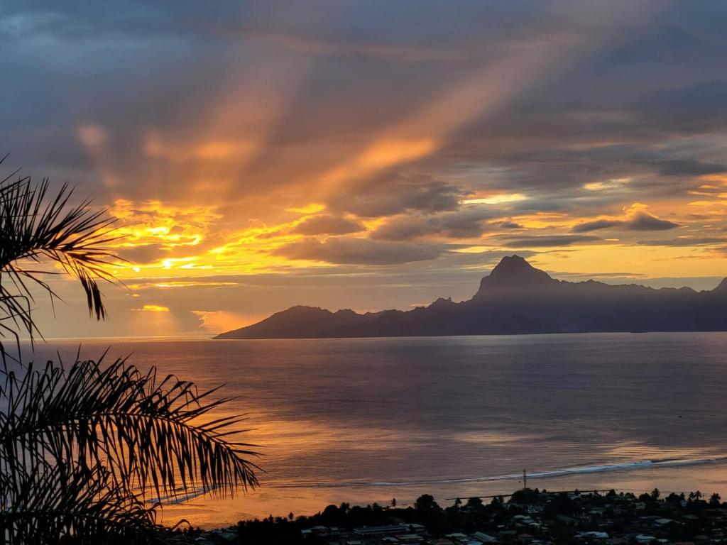 a sunset over the ocean with a mountain in the background at AU SOLEIL COUCHANT in Punaauia