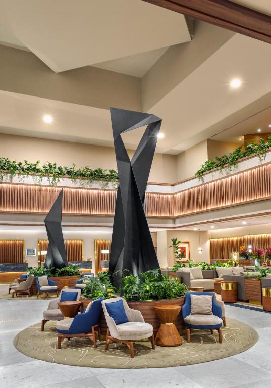 A grand lobby lounge arranged around a tall abstract sculpture and indoor planting.