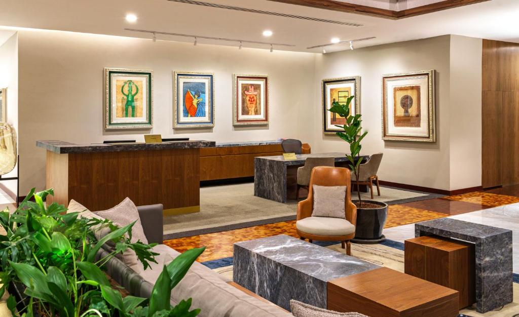 A polished lobby lounge with a reception desk, seating, artwork, and indoor plants.