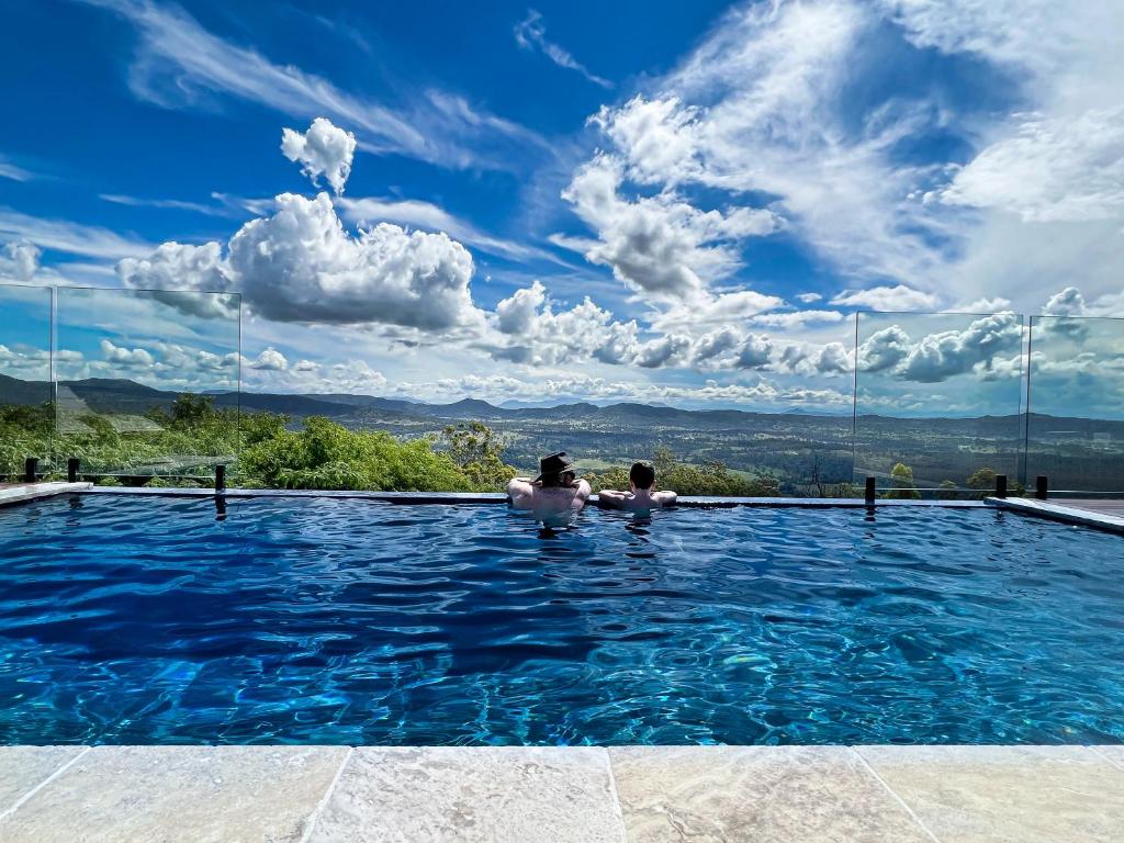 two people in a swimming pool with a view at Luxurious Hinterland Guest House with HEATED POOL Sleeps 10 Brisbane Scenic Rim Gold Coast in Canungra