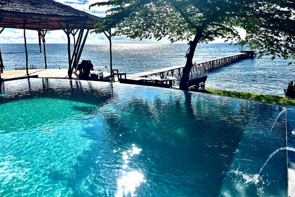 Sanctum Una Una Eco Dive Resort في Pulau Unauna: مسبح كبير بجانب الماء مع وجود شخص جالس