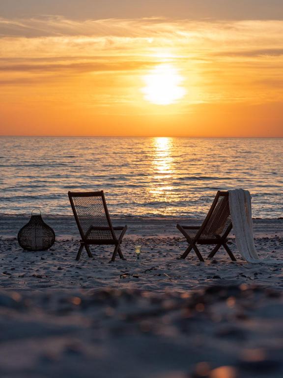 Zwei Strandstühle stehen bei Sonnenuntergang am Strand. in der Unterkunft Skrablas Boutique Hotel in Rucava