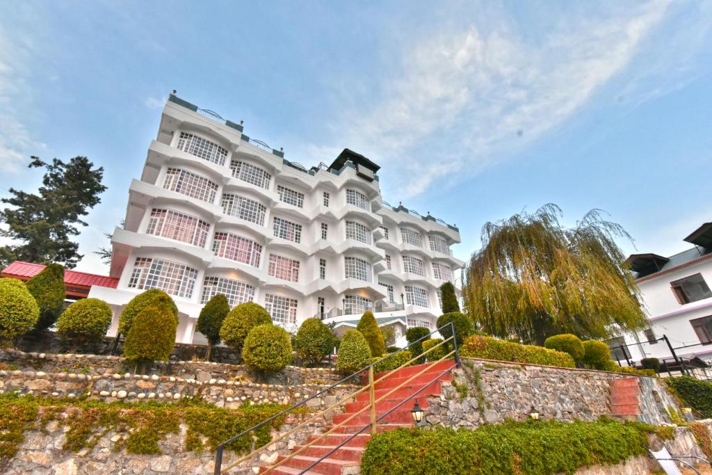 a large white building with bushes and trees at Hillcrest Resort by DLS Hotels in Shimla