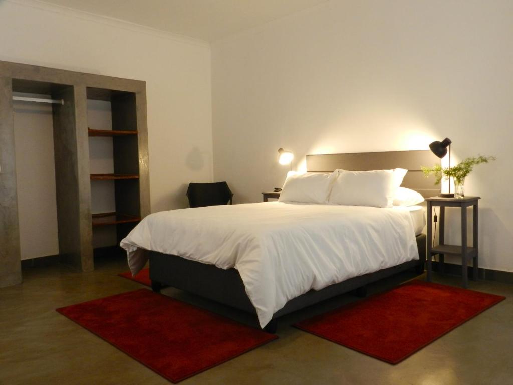 - une chambre avec un grand lit blanc et des tapis rouges dans l'établissement President Paul Kruger Guest Lodge, à Rustenburg