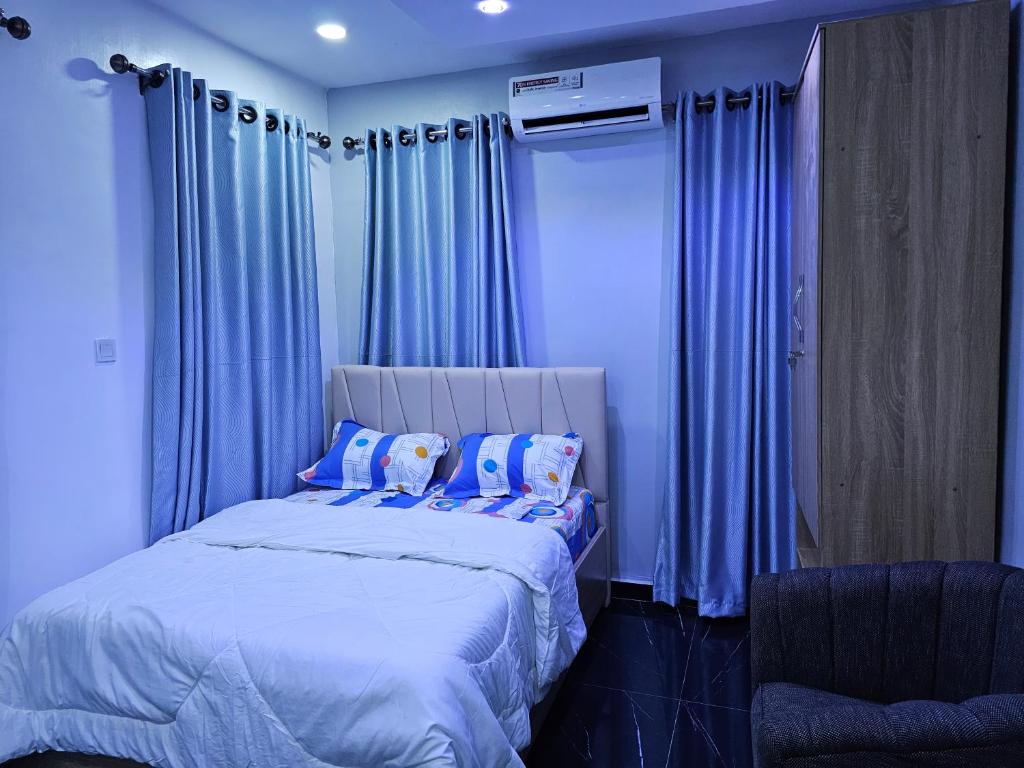 a bedroom with blue curtains and a large bed with pillows at HEN - CAP SERVICED APARTMETS in Agege