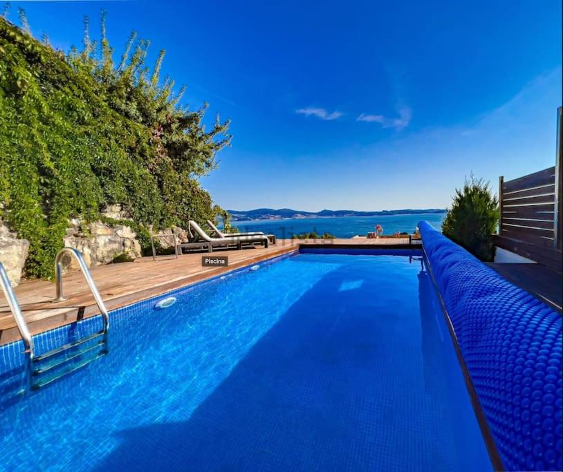 a blue swimming pool with a wooden deck and the water at Villa mirador de Sanxenxo in Sanxenxo