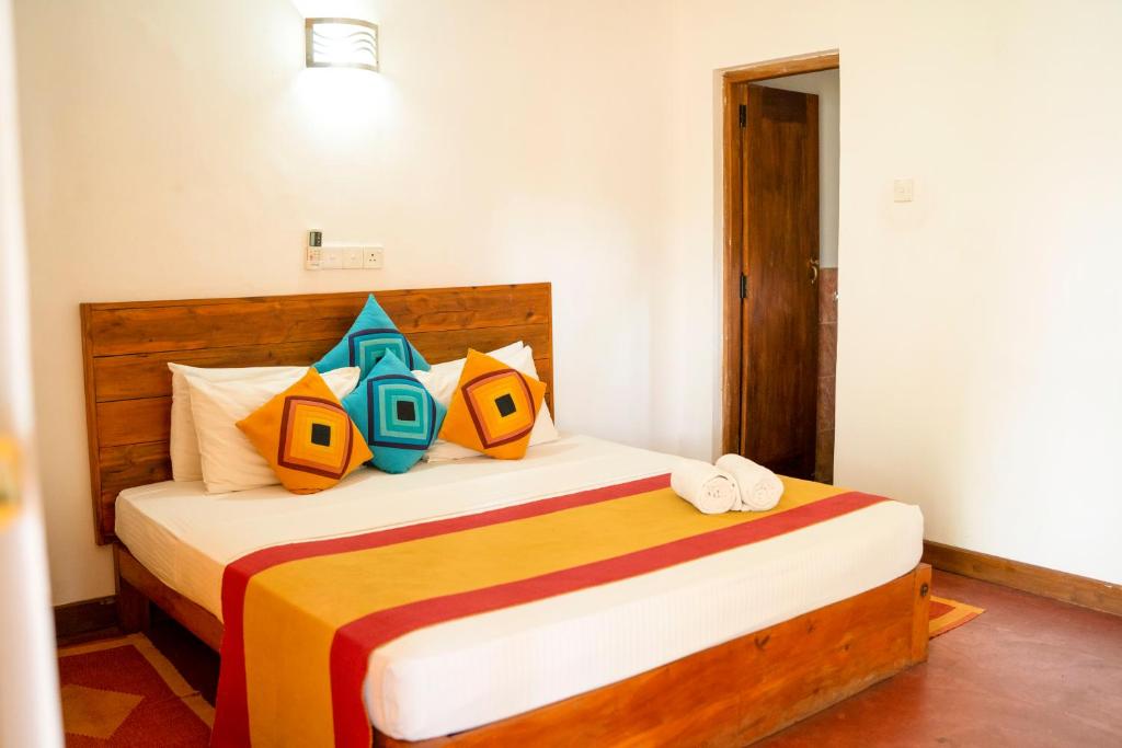 Wild Hut Habarana في هارابانا: غرفة نوم مع سرير كبير مع وسائد ملونة