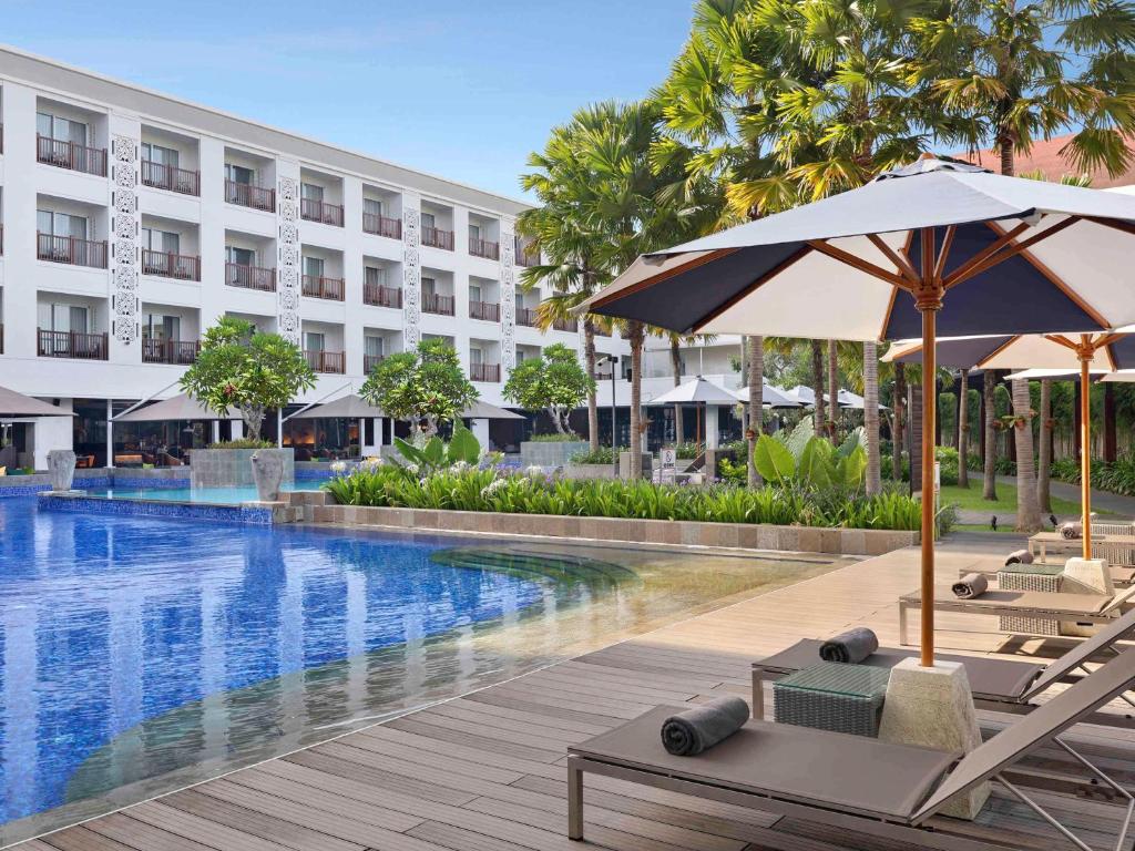 a hotel with a swimming pool with chairs and umbrellas at Grand Mercure Bali Seminyak in Seminyak