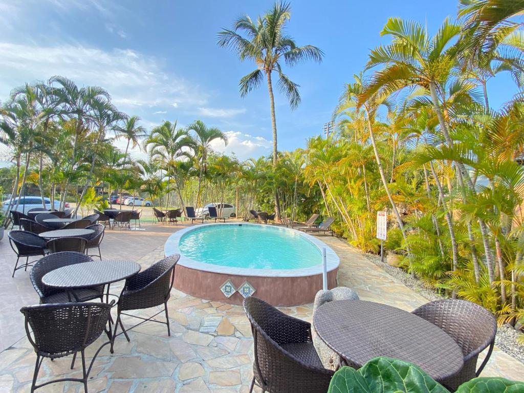 un complejo de piscina con mesas, sillas y palmeras en Pousada Montemar, en Ilhabela