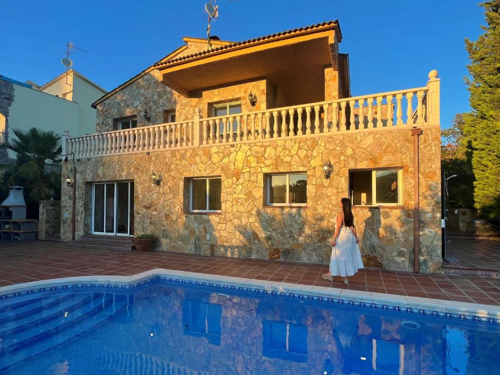 Una mujer con un vestido blanco parada frente a una casa en Encantadora casa rustica con piscina privada, en Palafolls