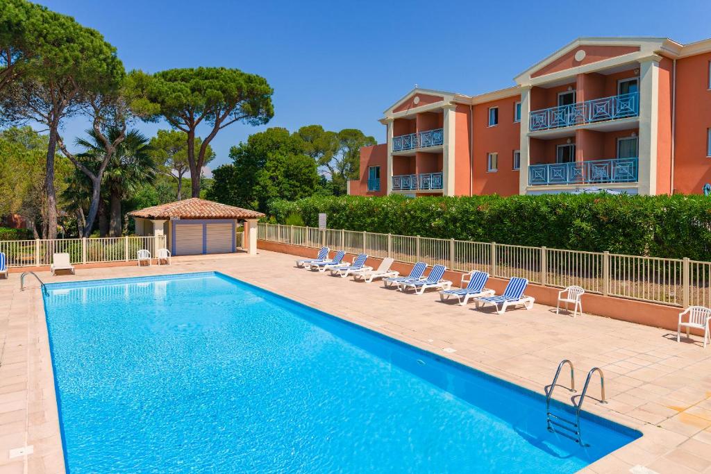 une piscine avec des chaises et un bâtiment dans l'établissement Lagrange Vacances Le Domaine des Grands Pins, à Saint-Raphaël