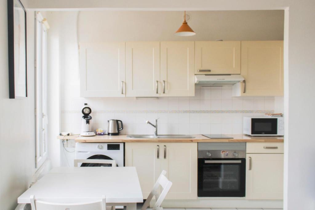 Le Pré-Saint-GervaisにあるWell Equipped 40m Apartment Near Parisの白いキッチン(白いキャビネット、テーブル付)