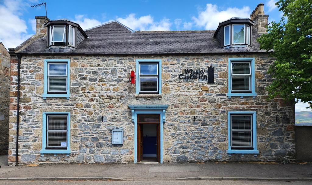 een oud stenen huis met blauwe ramen en een deur bij Whisky Capital Inn in Dufftown