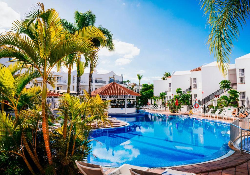 einen Pool in einem Resort mit Palmen und Stühlen in der Unterkunft Apartamentos Parque del Sol in Adeje