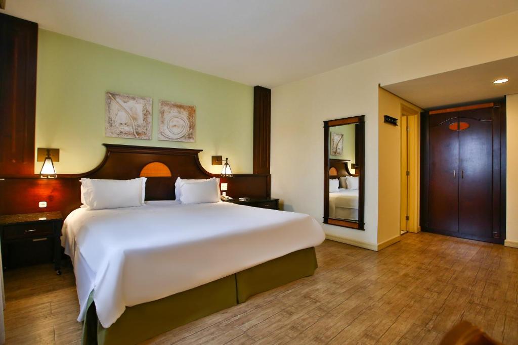 a bedroom with a large white bed and a mirror at Transamerica Prime Batel Curitiba in Curitiba