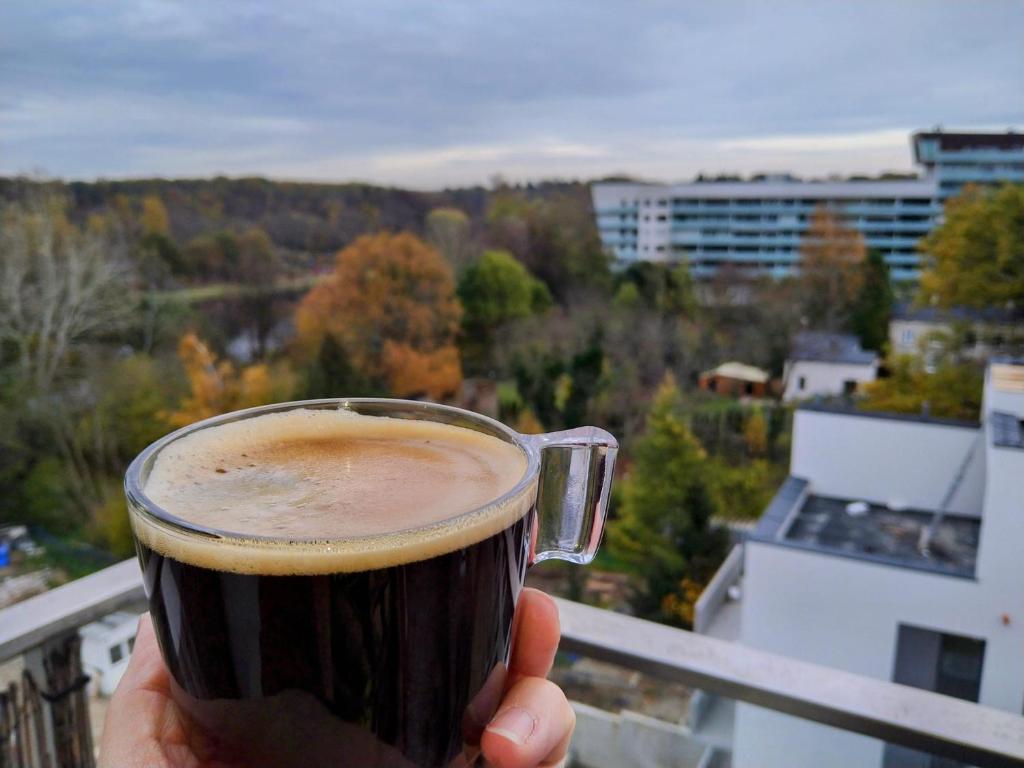 una persona che tiene una tazza di caffè sul balcone di Przytulny apartament z parkingiem a Łódź
