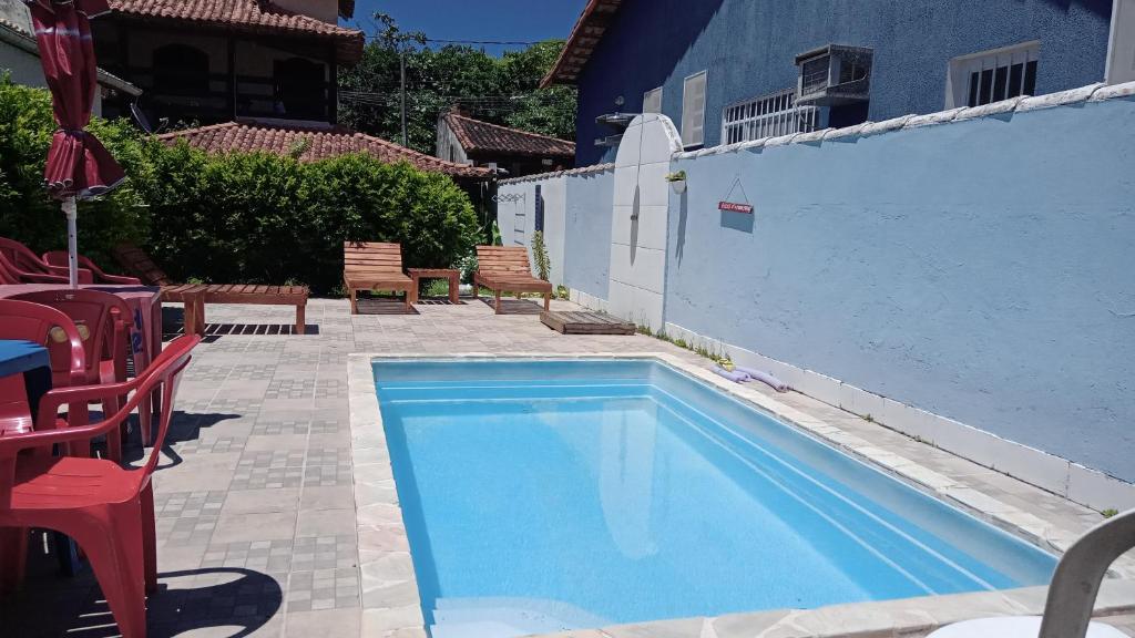 una piscina con sillas rojas y una pared azul en Caiçaras Búzios en Búzios