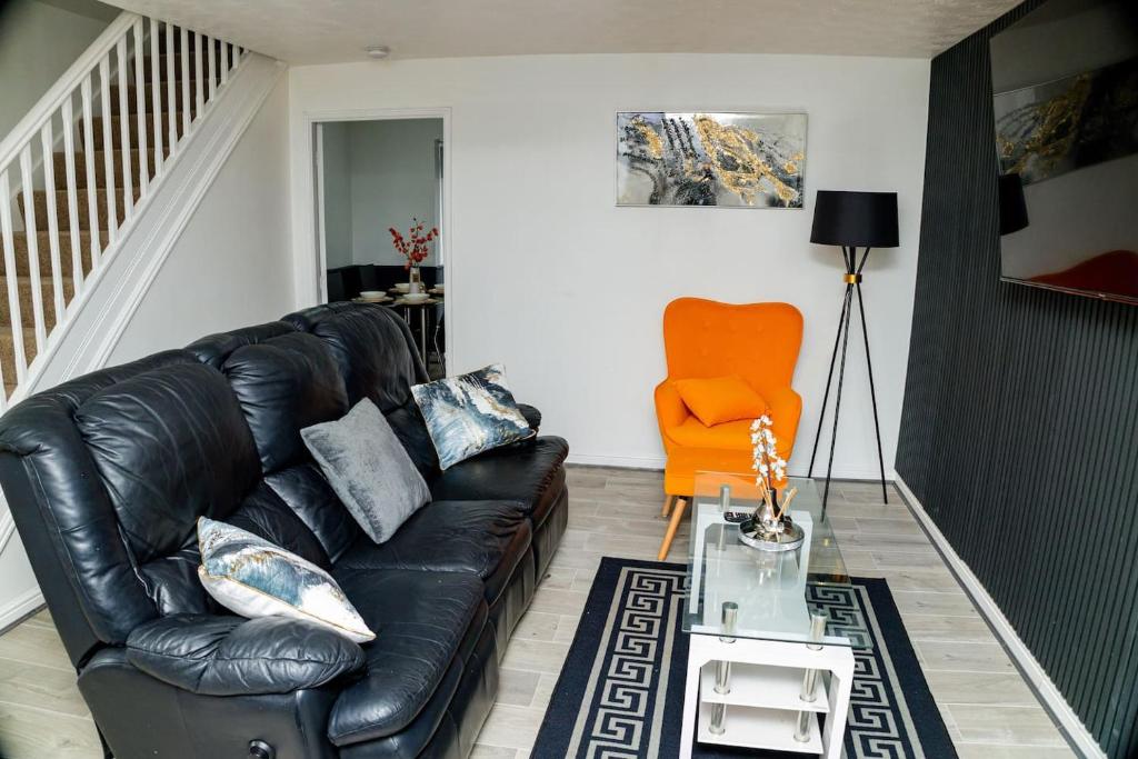 a living room with a black leather couch and an orange chair at Dynasty Lodge Manchester - Alison Kelly close in Manchester