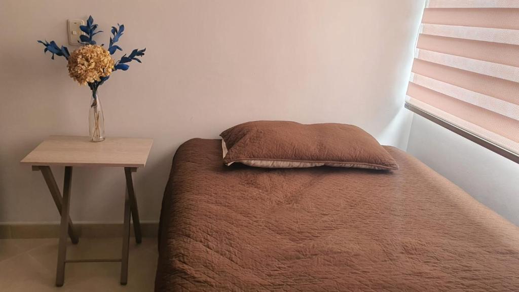 una cama con un jarrón de flores junto a una mesa en Habitación en apartamento compartido en Envigado en Envigado