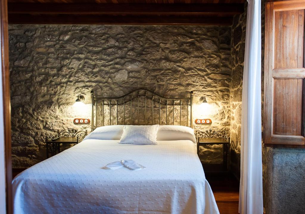 1 dormitorio con 1 cama blanca grande y pared de piedra en Casa de Costoia, en Santiago de Compostela