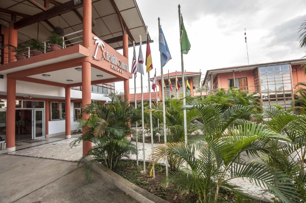 un bâtiment avec des drapeaux et des palmiers devant lui dans l'établissement Hotel Cabaña Quinta, à Puerto Maldonado