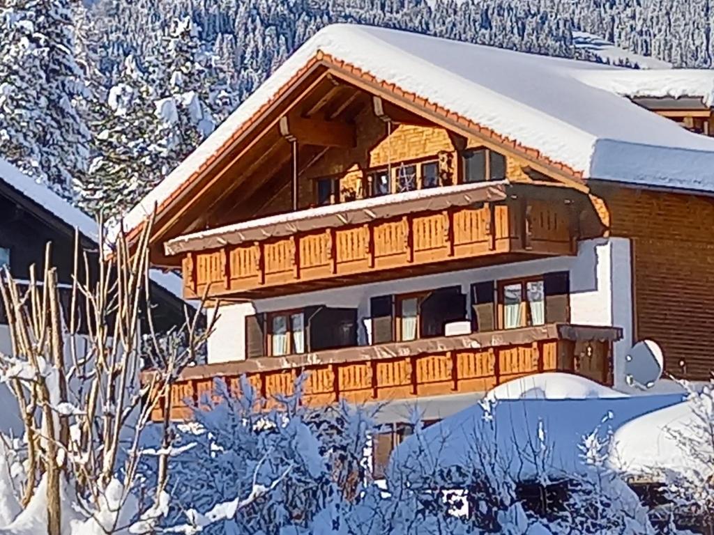 ein schneebedecktes Haus mit Bäumen im Hintergrund in der Unterkunft Gästehaus Schmid in Obermaiselstein