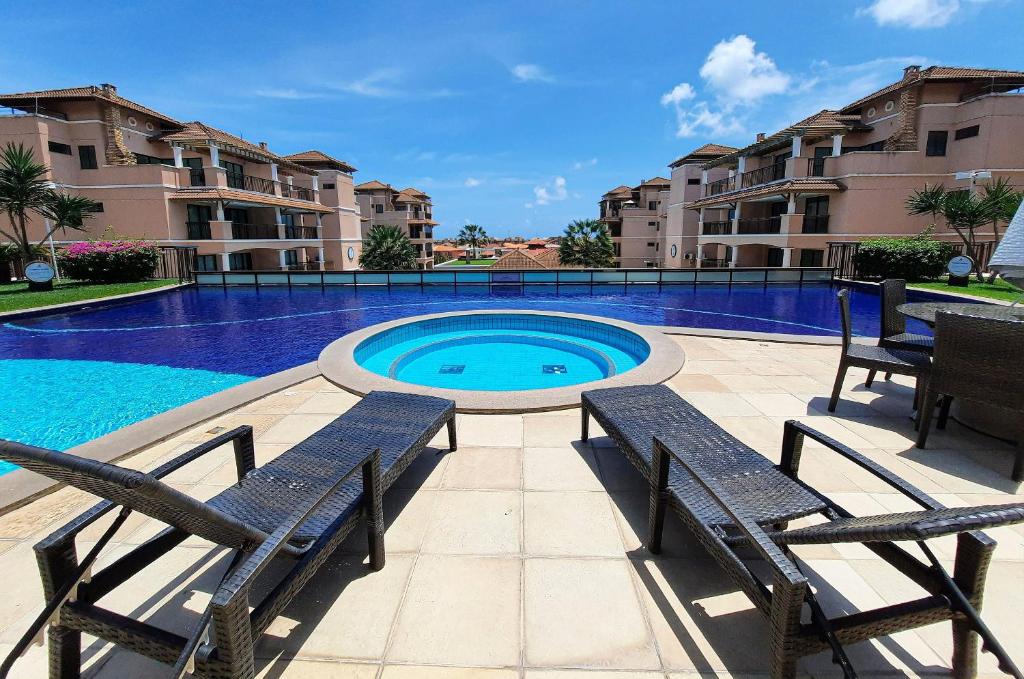 a swimming pool with two benches in front of some buildings at Beverly Hills 2 Suítes Apto Completo 500m Praia in Aquiraz