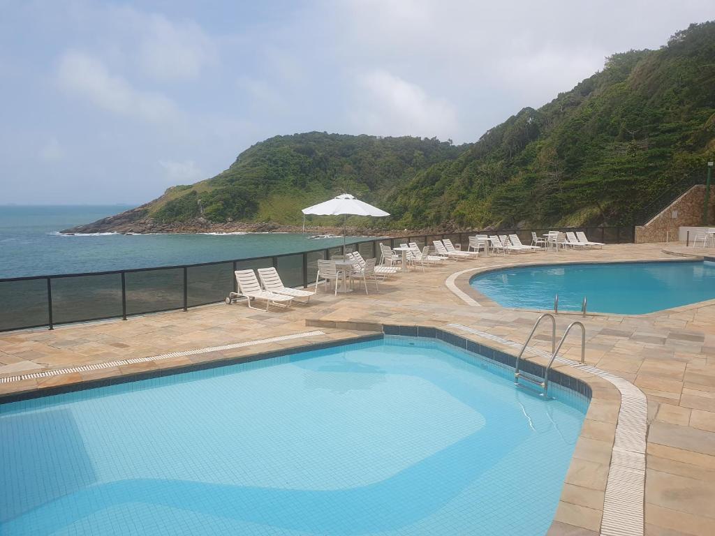 una piscina con sillas y vistas al océano en APARTAMENTO EM CONDOMÍNIO- acolhedor-FRENTE MAR-ENSEADA-TORTUGA, en Guarujá