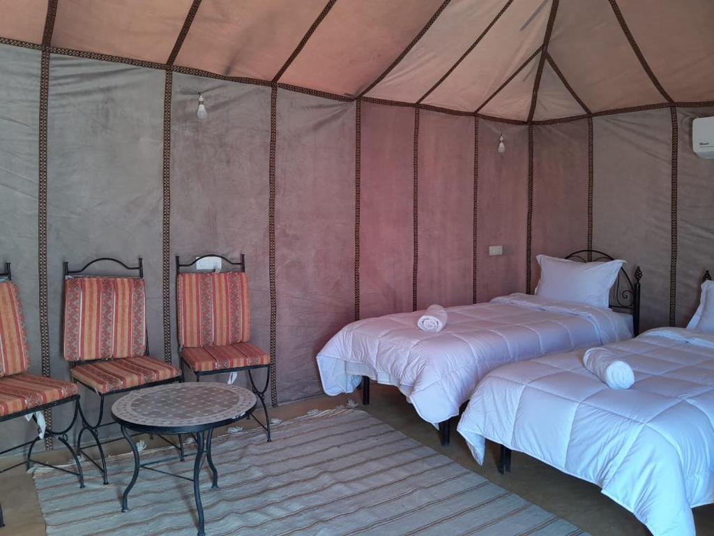 Adrouineにあるmerzouga berber tentsのベッド2台、テーブル、椅子が備わる客室です。