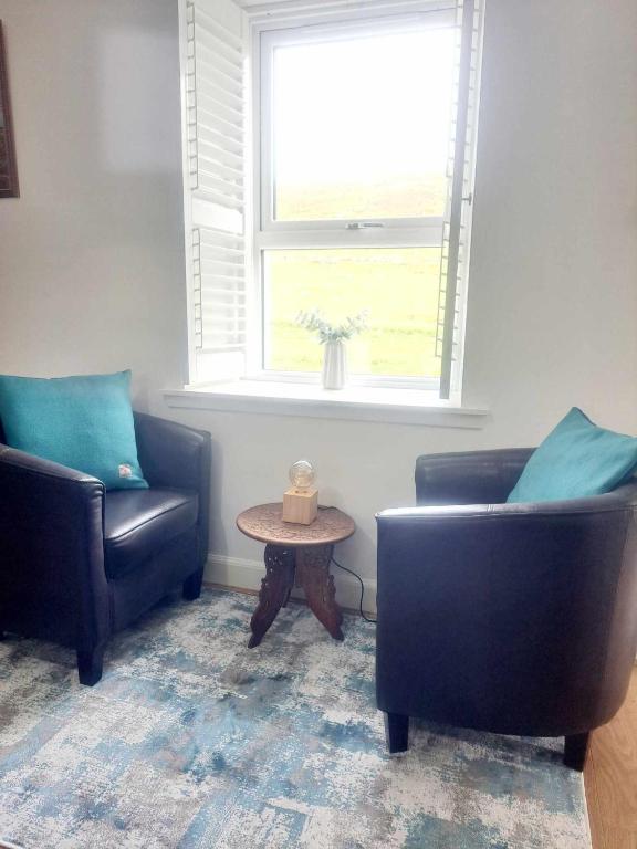a living room with two chairs and a table and a window at Cliff Cottage in Valtos