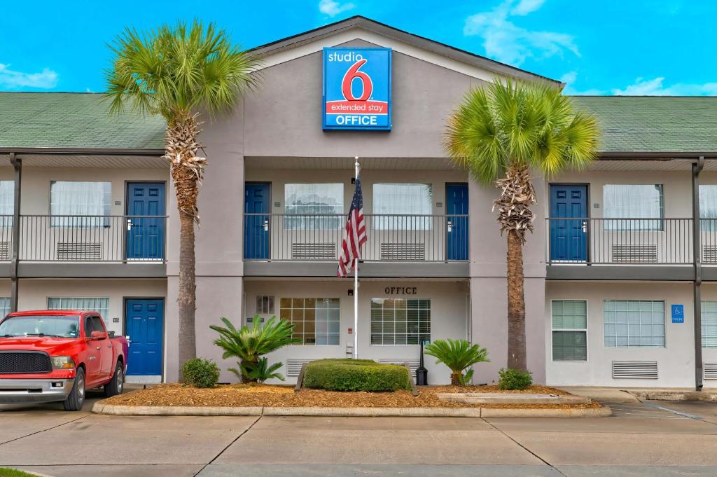 un camión rojo estacionado frente a un hotel con palmeras en Studio 6-Pascagoula, MS, en Pascagoula