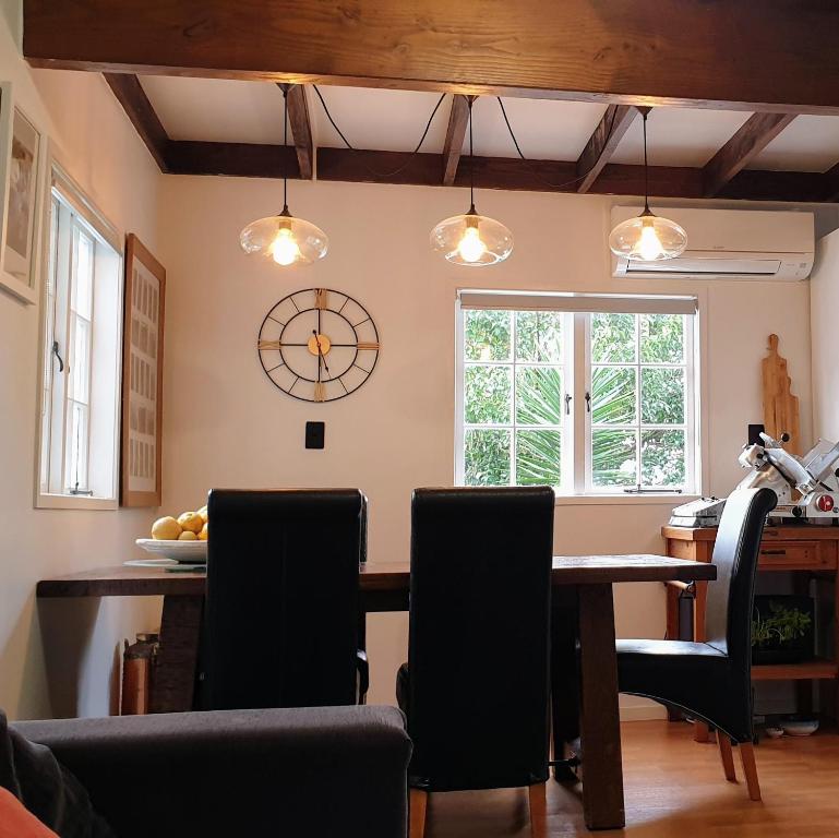 a dining room table with chairs and a clock on the wall at Abbeygate Cottage in Auckland