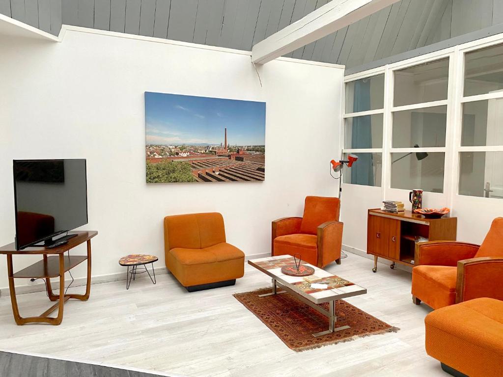 sala de estar con sillas de color naranja y TV en Le Loft des Musiciens, en Mulhouse