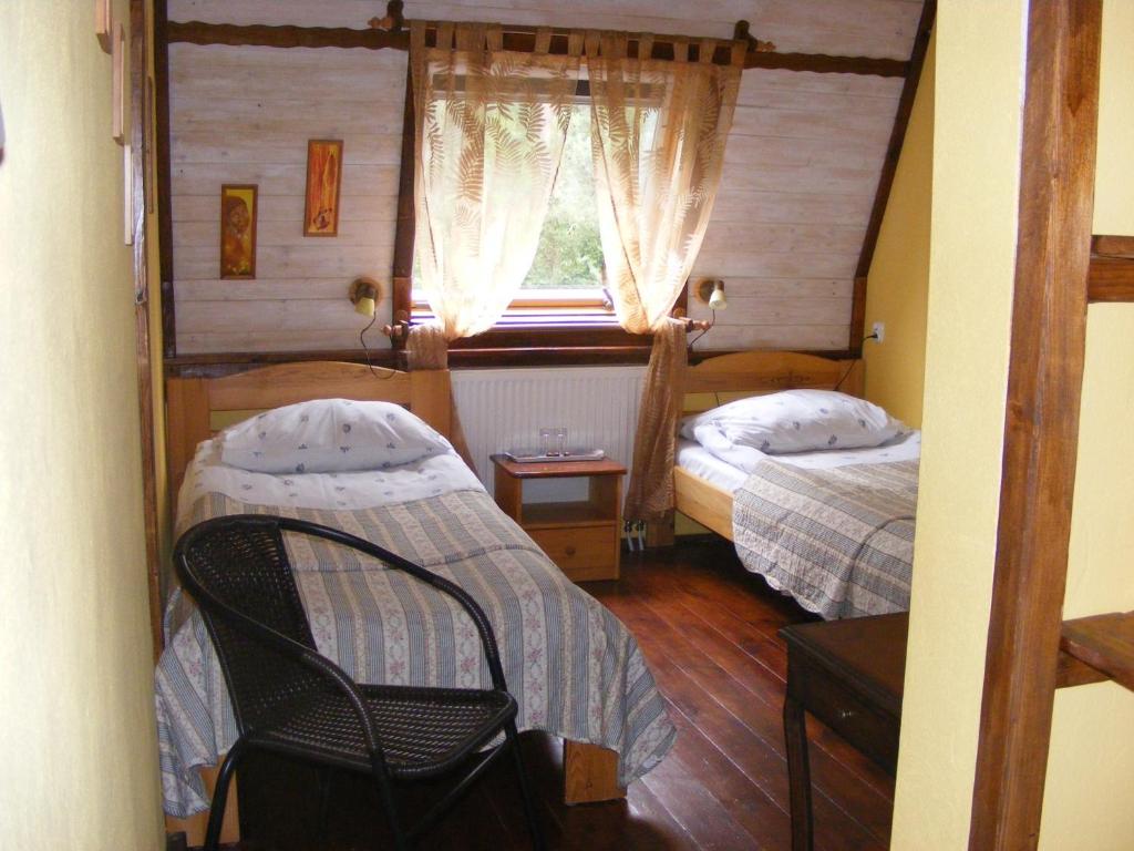 Attic twin bedroom with two beds, sheer curtains over window, wicker chair in foreground.