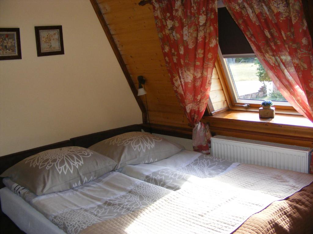 Sunlit double bed under sloped window, red floral curtains and wooden window ledge.