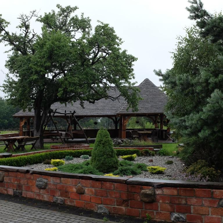Outdoor pavilion with wooden beams and picnic benches framed by mature trees and landscaped garden.