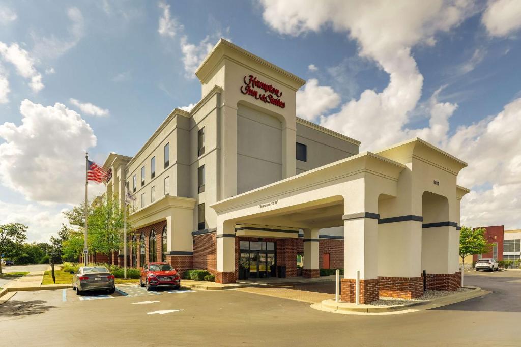 ein Hotelgebäude mit amerikanischer Flagge auf einem Parkplatz in der Unterkunft Hampton Inn & Suites Indianapolis-Airport in Indianapolis